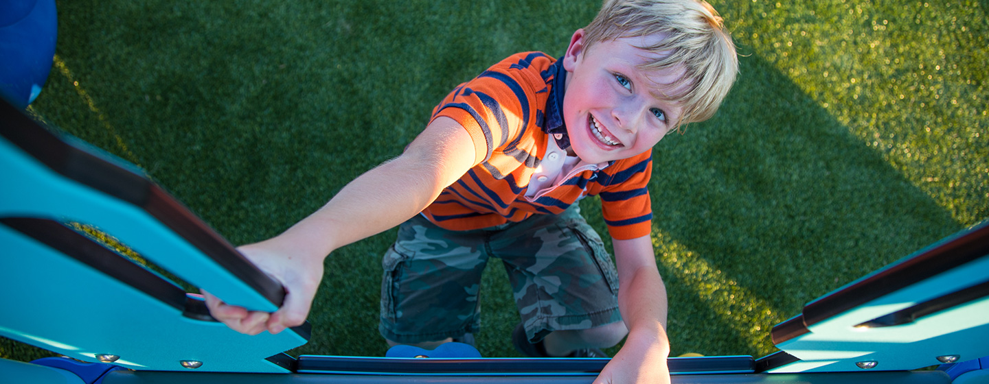 Boy with wide smile climbing up a playground climber with Permalene handholds.