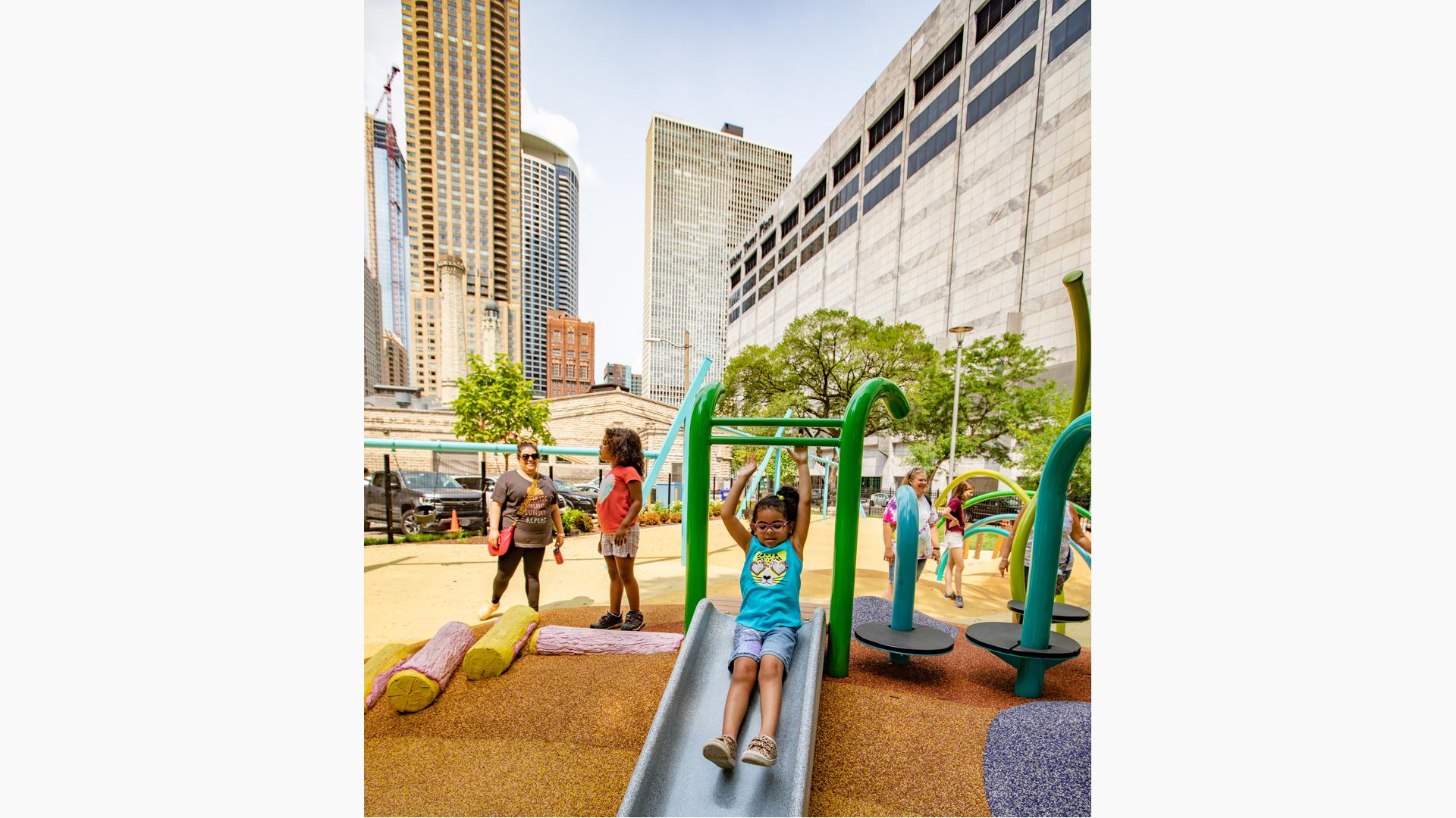 Girl riding slide with both arms up