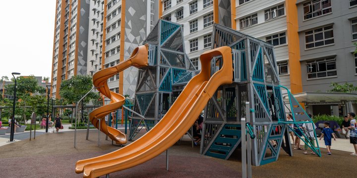 Two A-shaped playground towers with two orange slides descending from them, and city buildings in the background. 